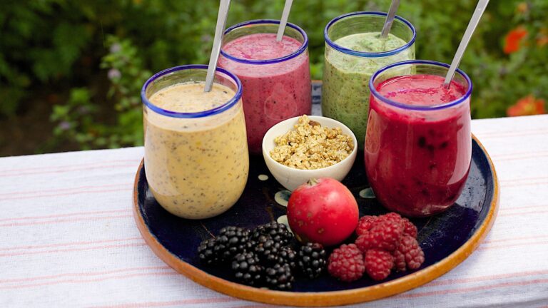 a set of 4 colorful smoothies in a tray with various fruits